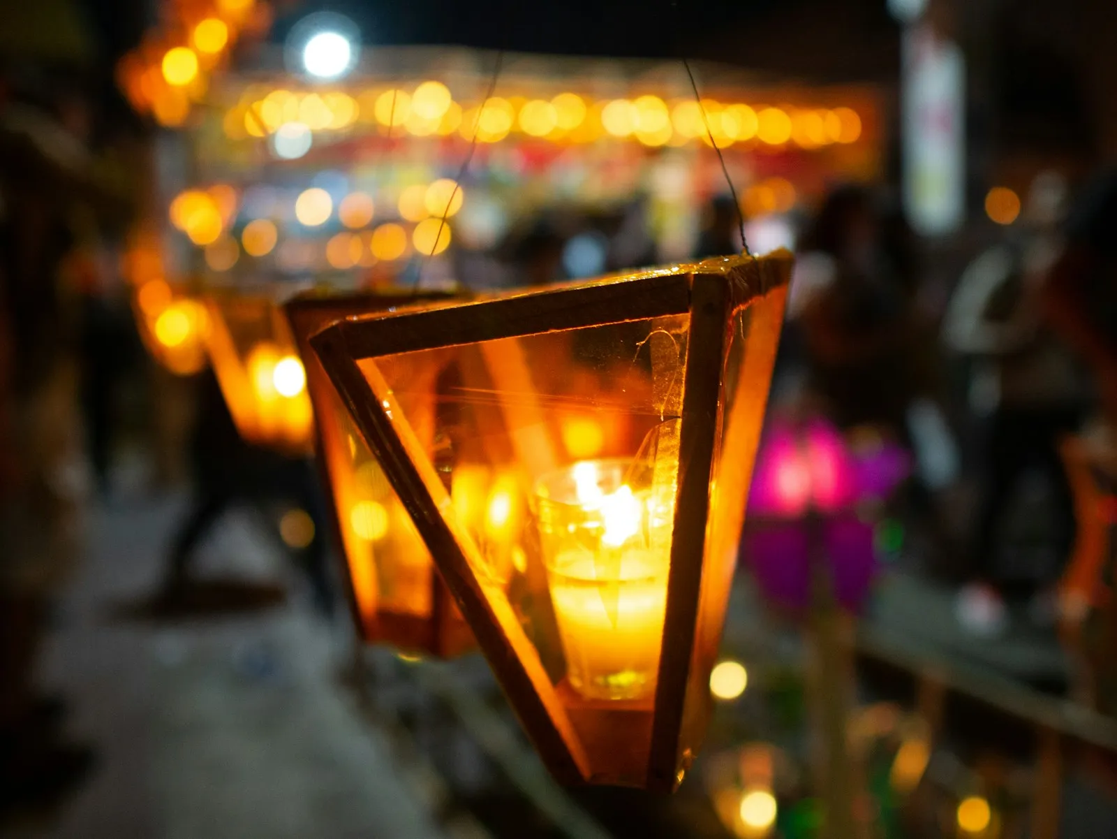 Farolito de papel celofán con una vela encendida colgado en una calle de Ahuachapán, con más farolitos y luces desenfocadas al fondo