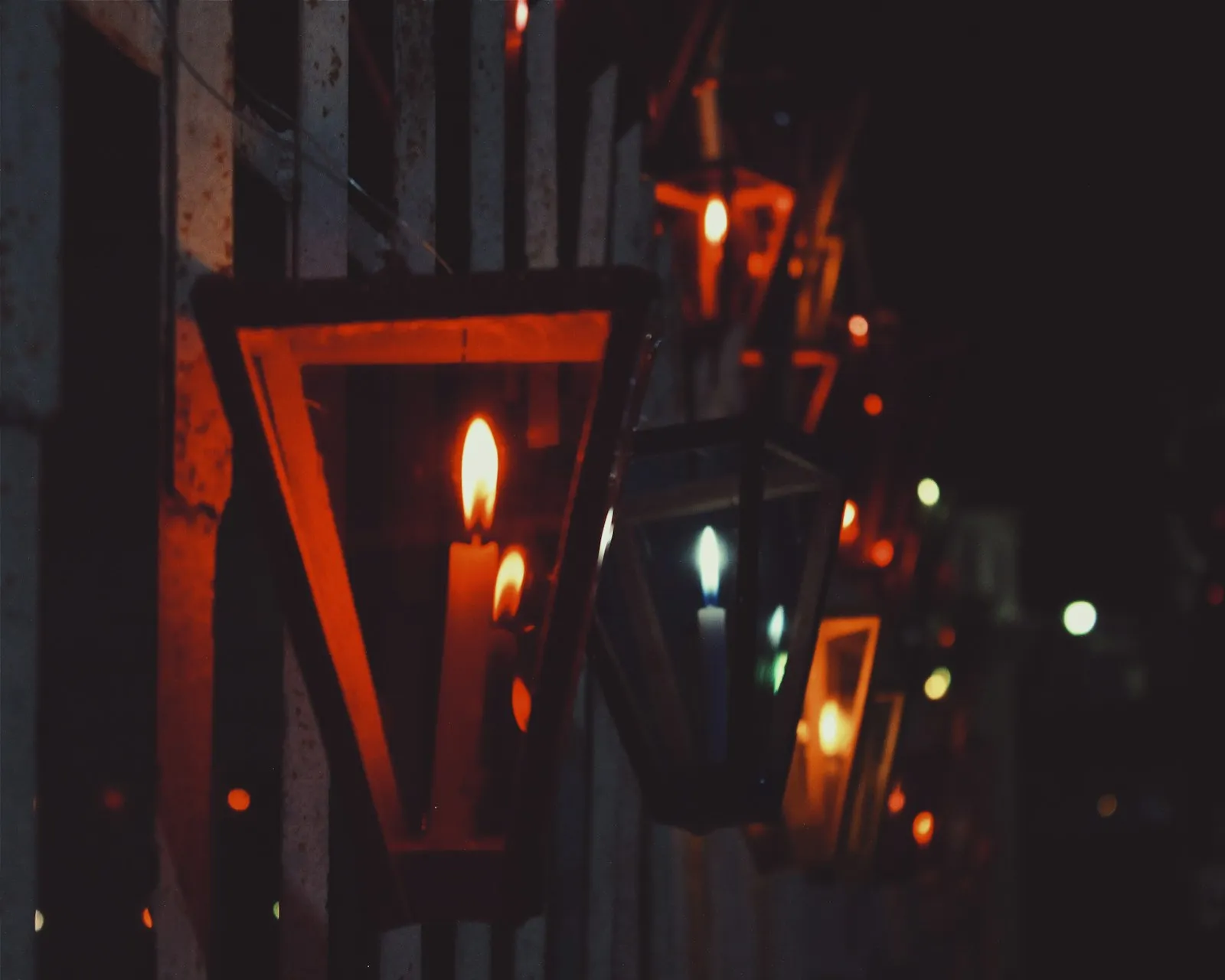 Hilera de farolitos de madera y celofán con velas encendidas colgados en la fachada de una casa de Ahuachapán durante la noche