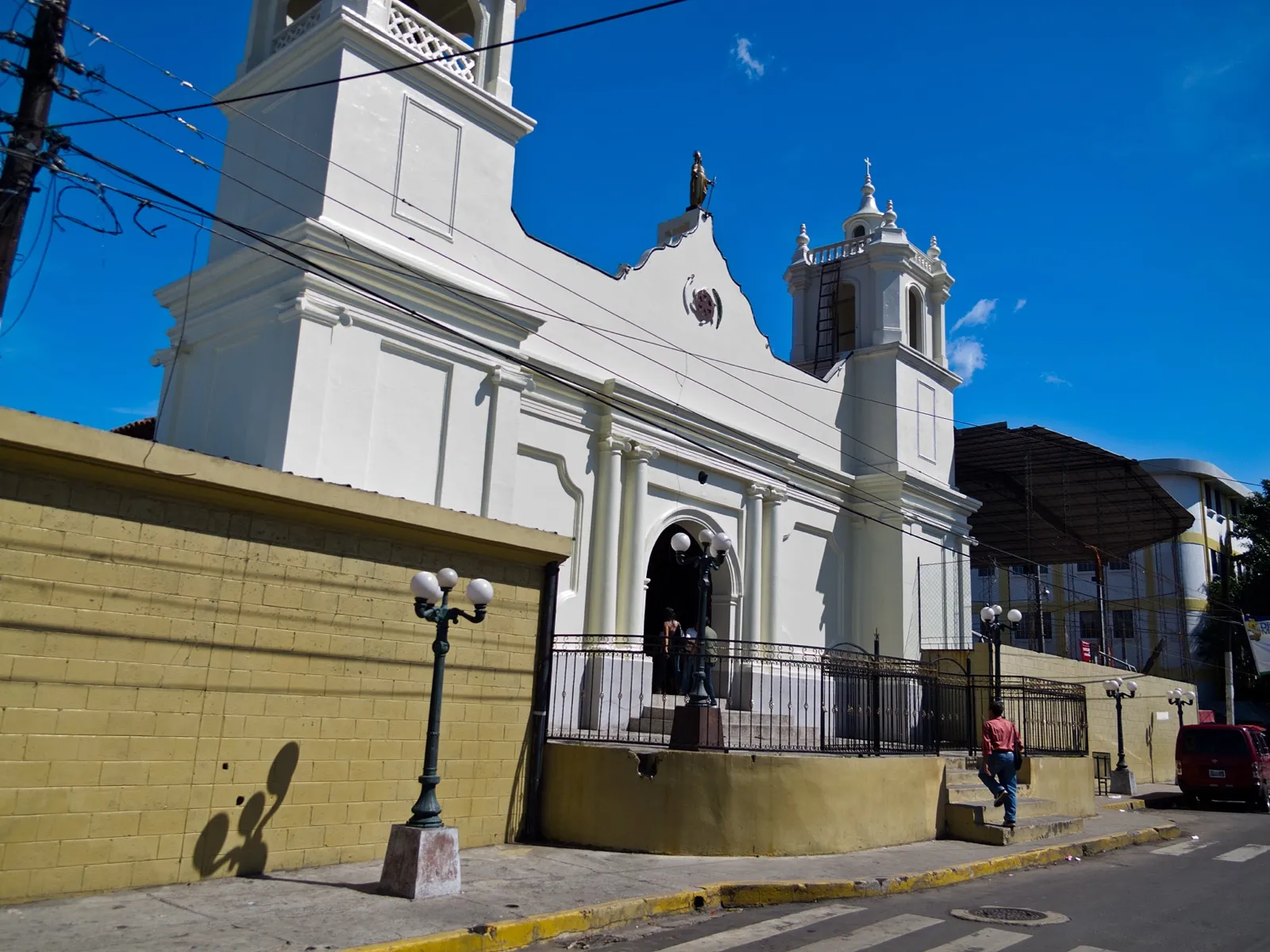 Iglesia parroquial blanca de Apopa con su torre, frente al parque central
